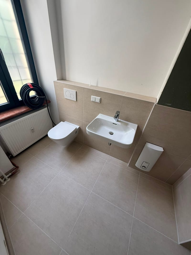 Helles fertiges Bad mit Hänge-WC, Waschbecken, Heizkörper und Fenster
