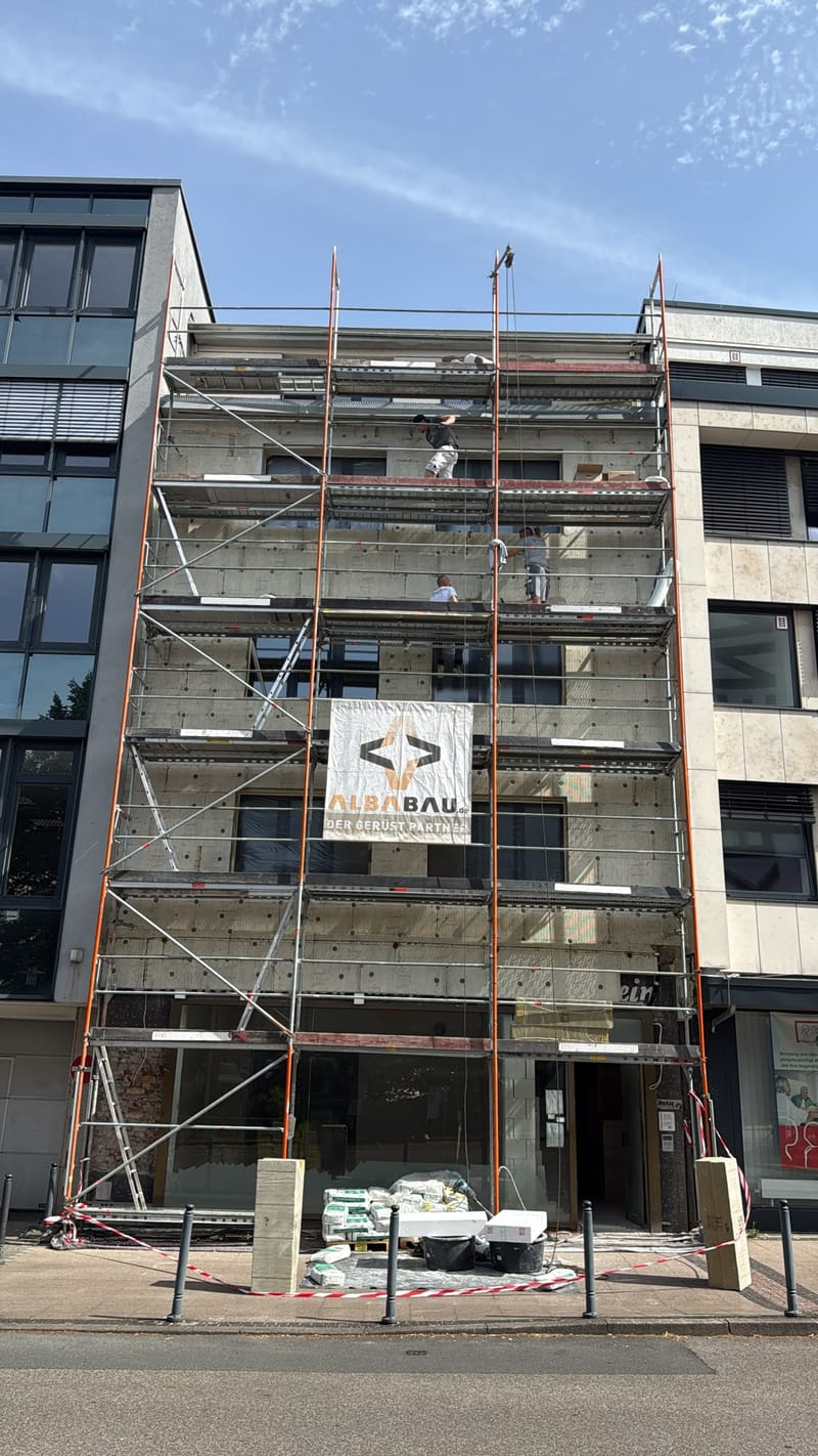 Frontale Gesamtansicht des eingerüsteten Stadthauses mit Arbeitern unter blauem Himmel